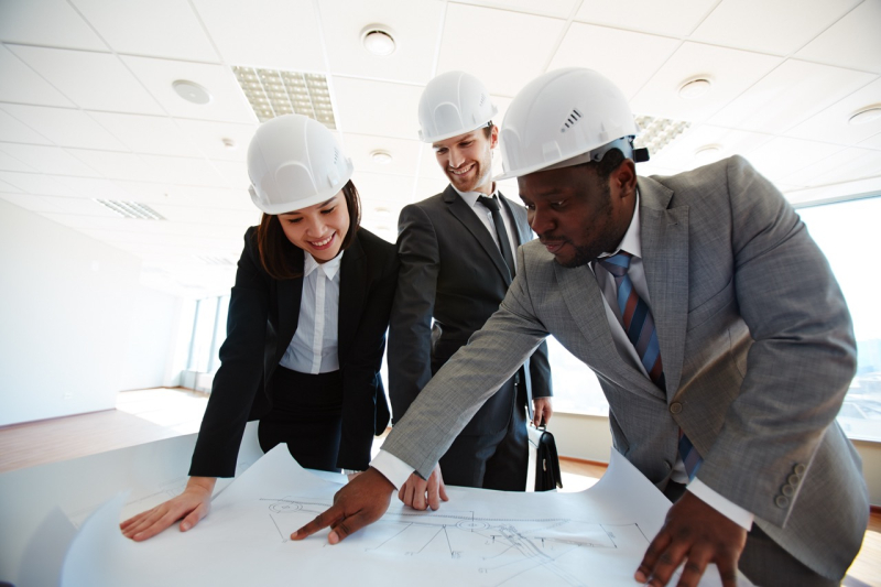 Confident architects in protective helmets looking at blueprint